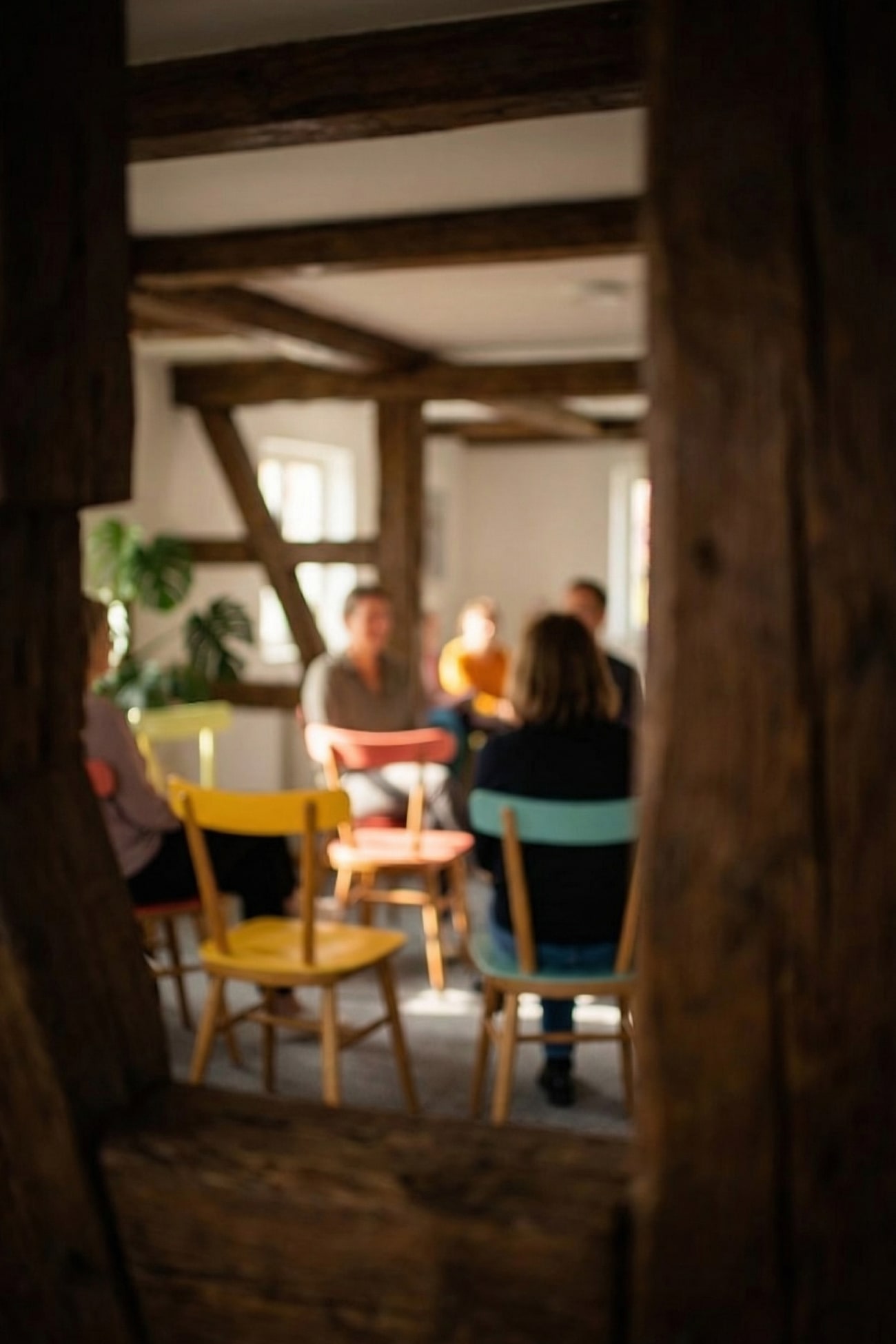 Eine Gruppe von Personen sitzt in einem Raum, umgeben von Holzstrukturen und bunten Stühlen.