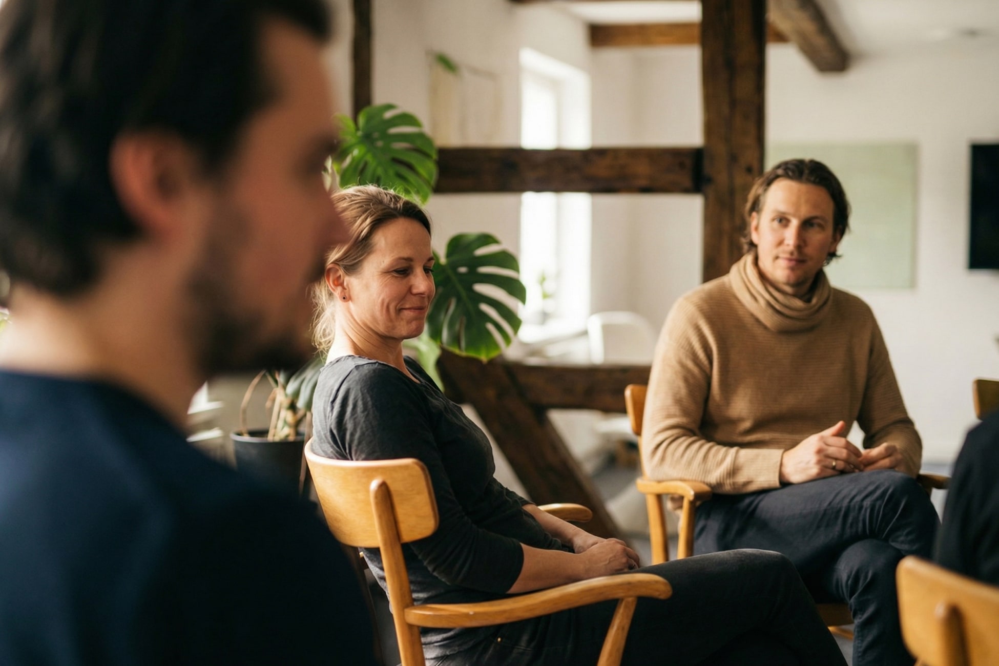 Eine Gruppe von drei Personen sitzt in einem hellen Raum und diskutiert, umgeben von Pflanzen und Holzdetails.