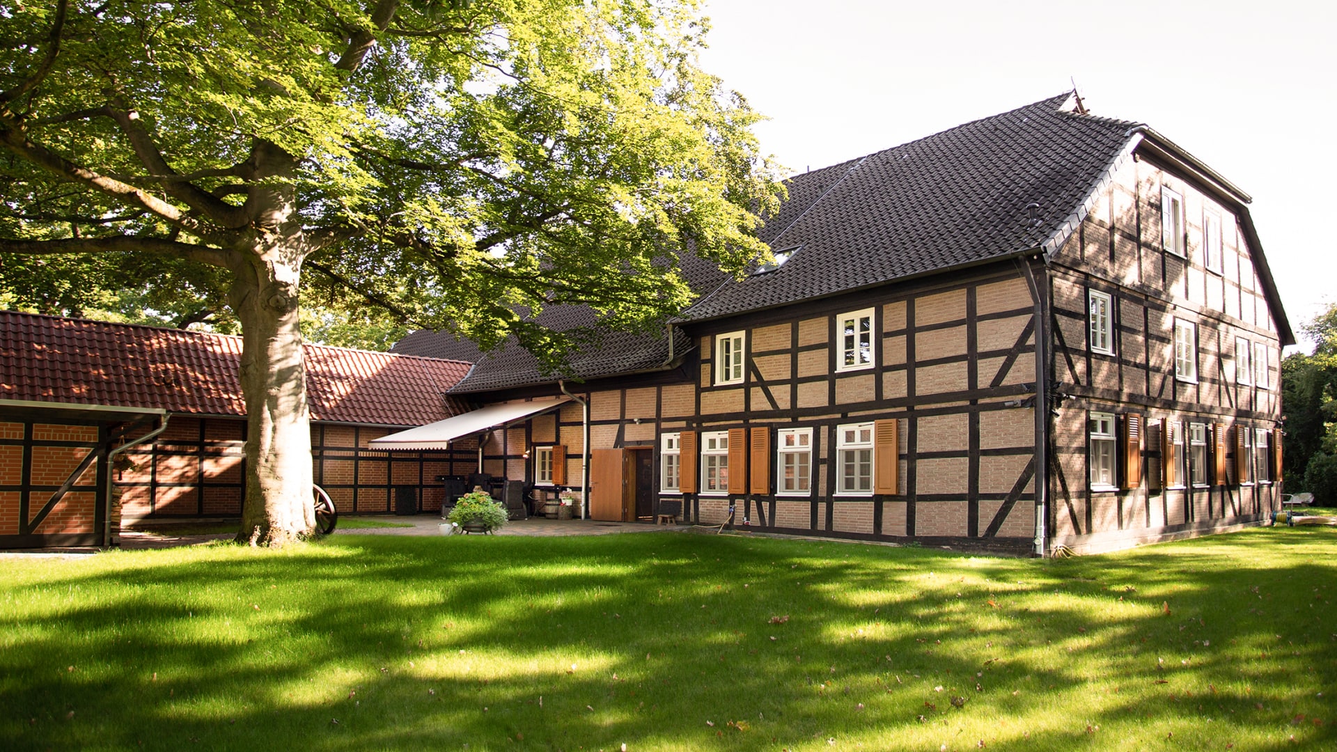 Historisches Fachwerkhaus mit grünem Rasen und großen Bäumen im Vordergrund.