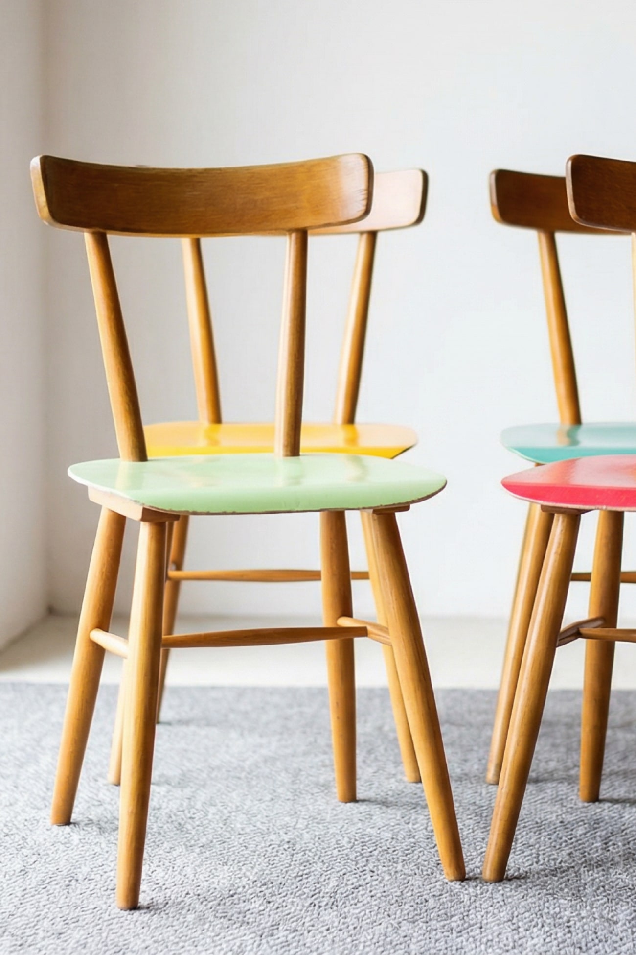 Bunte Küchenstühle aus Holz in einem modernen Stillleben auf einem grauen Teppich.