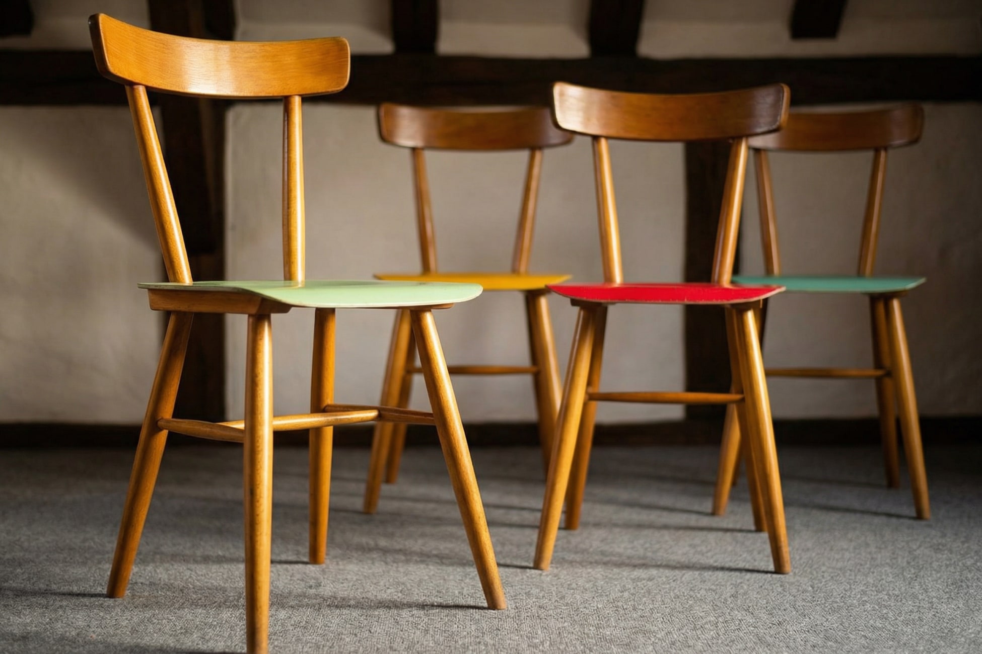 Stillleben mit vier Holzstühlen in verschiedenen Farben auf einem Teppichboden.