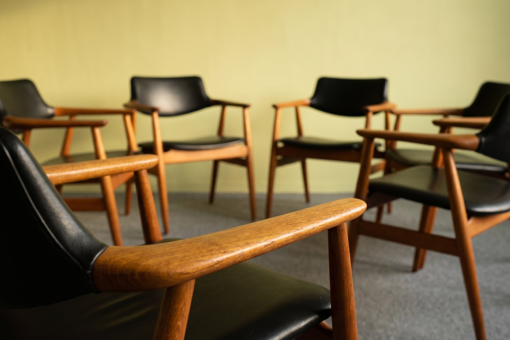 Stillleben mit mehreren schwarzen Seminarstühlen aus Holz vor einer hellgrünen Wand.